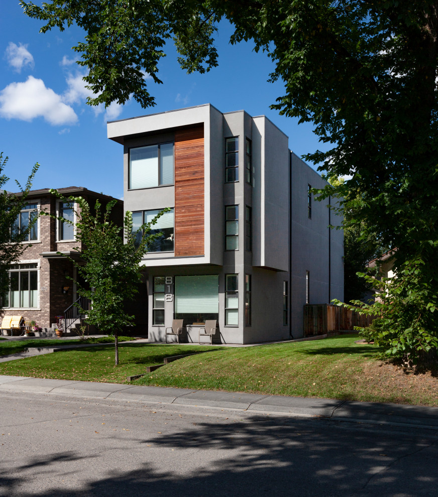 Contemporary three-storey stucco grey house exterior in Calgary with a flat roof.