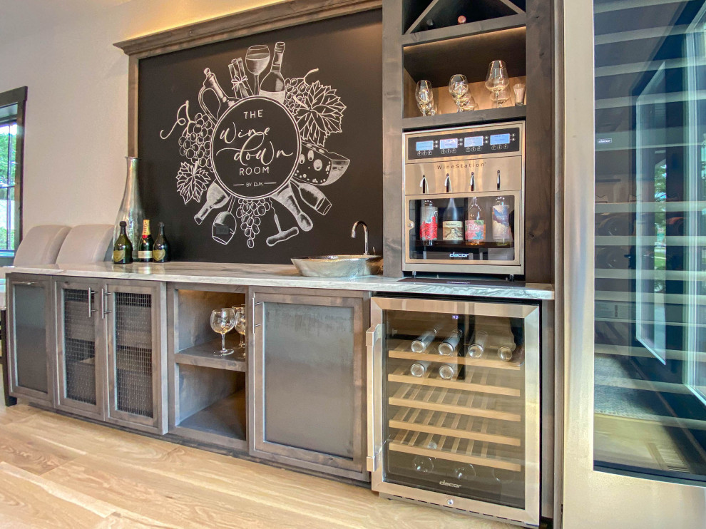 Large contemporary single-wall wet bar in Chicago with an integrated sink, shaker cabinets, distressed cabinets, quartzite benchtops, black splashback, light hardwood floors and white benchtop.