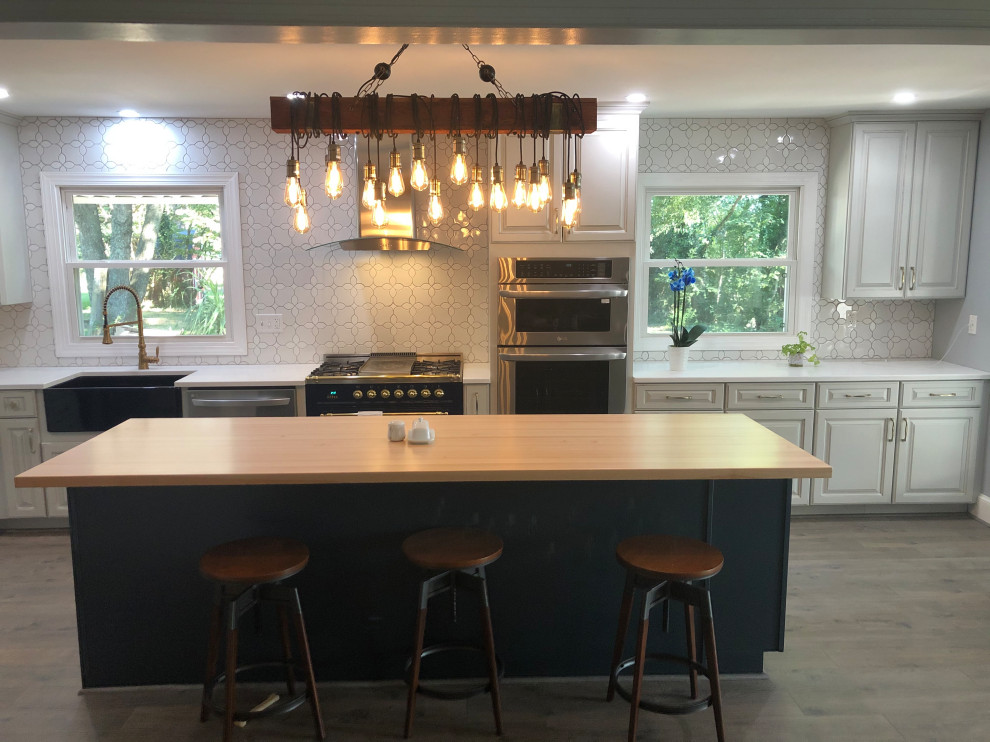 Example of a mid-sized transitional l-shaped vinyl floor and brown floor kitchen design in DC Metro with a farmhouse sink, raised-panel cabinets, gray cabinets, solid surface countertops, white backsplash, ceramic backsplash, stainless steel appliances, an island and white countertops