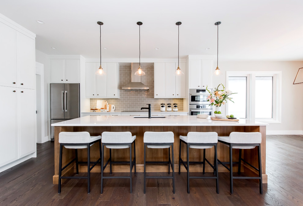 Inspiration for a large transitional l-shaped separate kitchen in Calgary with a double-bowl sink, raised-panel cabinets, quartz benchtops, grey splashback, stainless steel appliances, medium hardwood floors, with island and subway tile splashback.