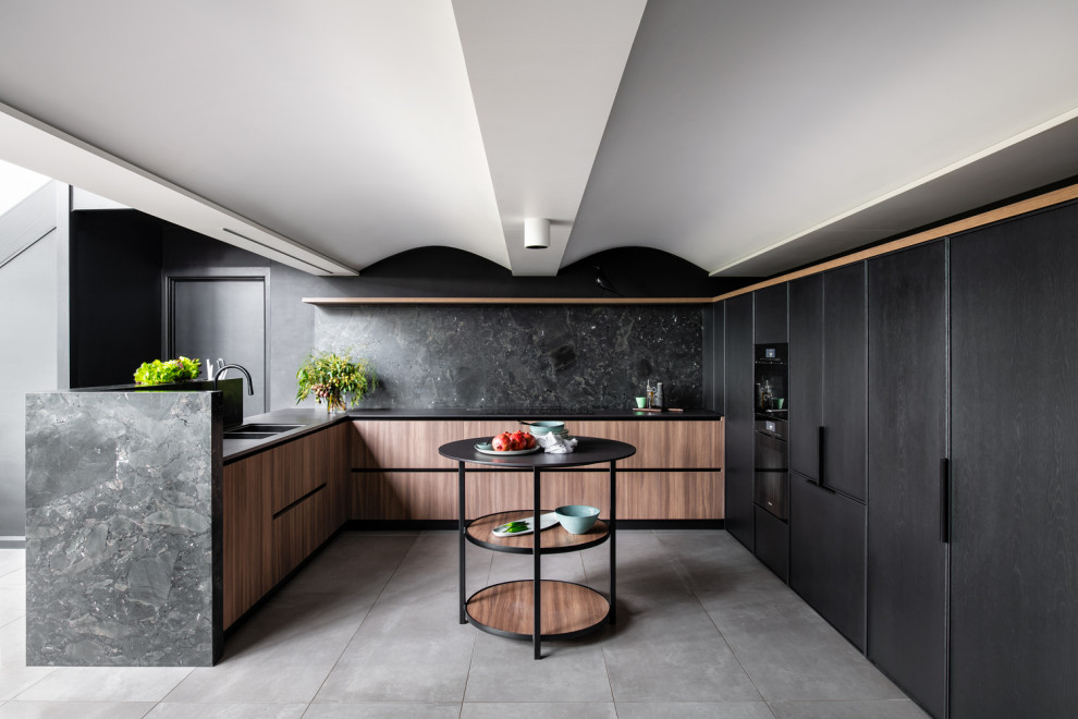 Design ideas for a mid-sized contemporary u-shaped open plan kitchen in Sydney with an undermount sink, recessed-panel cabinets, black splashback, stone slab splashback, black appliances, porcelain floors, with island, black benchtop and wood.