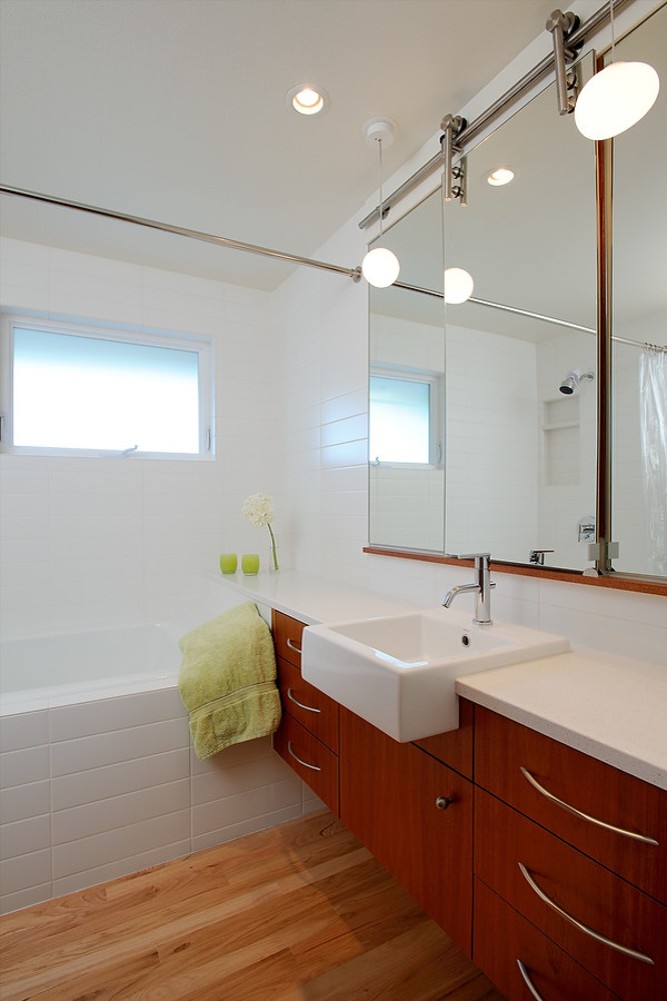 Design ideas for a mid-sized contemporary master bathroom in Seattle with a drop-in sink, flat-panel cabinets, medium wood cabinets, engineered quartz benchtops, a drop-in tub, a shower/bathtub combo, a two-piece toilet, white tile, ceramic tile, white walls and light hardwood floors.