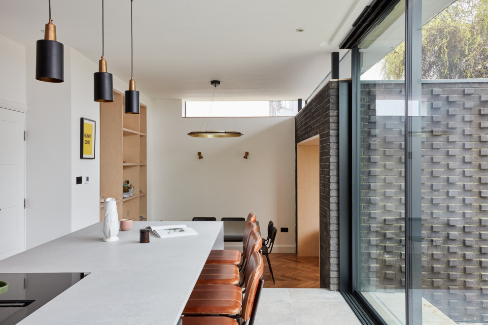 This is an example of a large contemporary l-shaped open plan kitchen in London with an undermount sink, flat-panel cabinets, light wood cabinets, quartz benchtops, white splashback, engineered quartz splashback, stainless steel appliances, limestone floors, with island, grey floor and white benchtop.