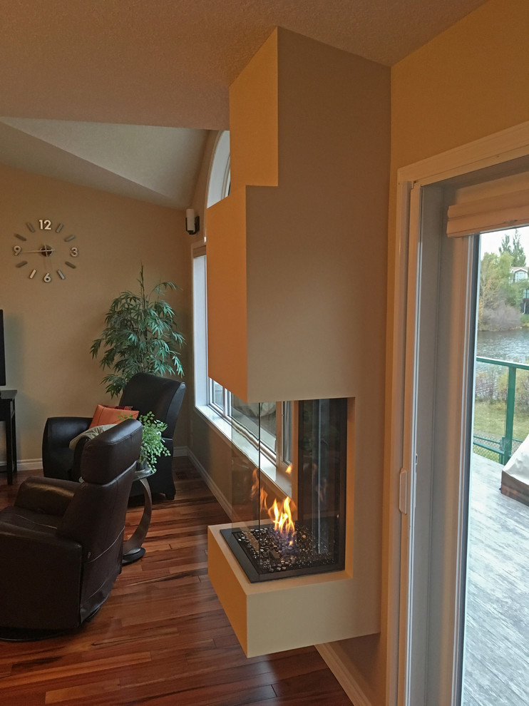 This is an example of a mid-sized traditional enclosed living room in Edmonton with beige walls, dark hardwood floors, a hanging fireplace, a plaster fireplace surround and brown floor.