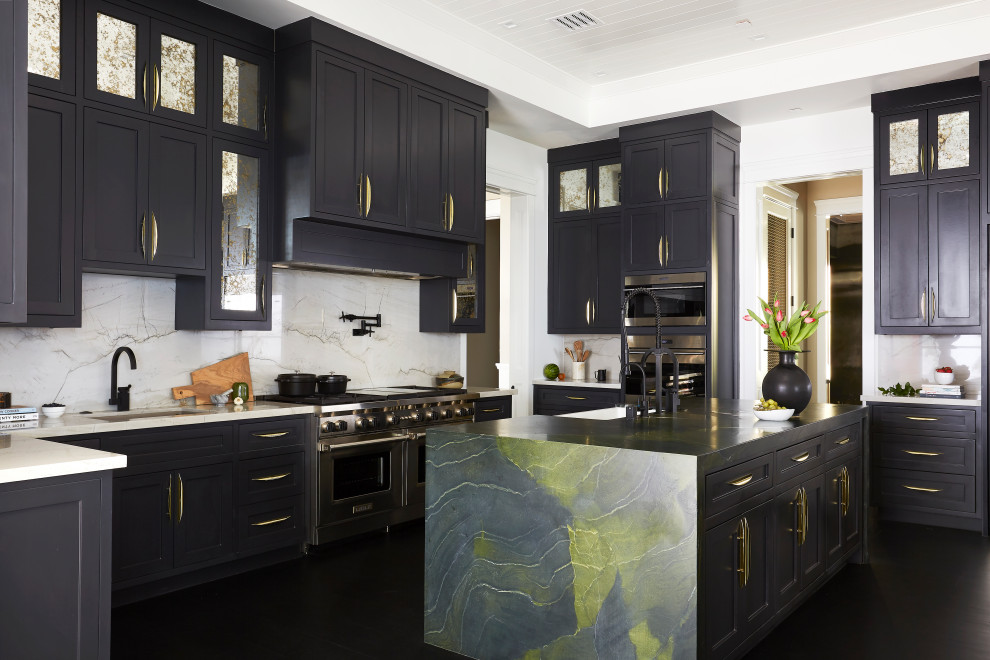 Design ideas for an expansive transitional u-shaped kitchen in Los Angeles with a farmhouse sink, shaker cabinets, black cabinets, white splashback, stainless steel appliances, with island, black floor and white benchtop.