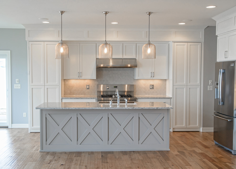 Kitchen - mid-sized rustic l-shaped medium tone wood floor and brown floor kitchen idea with a farmhouse sink, shaker cabinets, white cabinets, granite countertops, brown backsplash, porcelain backsplash, stainless steel appliances and an island