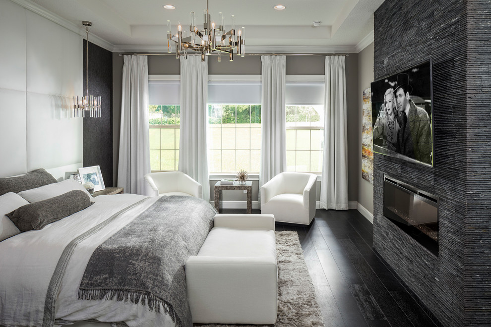 Transitional bedroom in Orlando with grey walls, dark hardwood floors, a ribbon fireplace, a stone fireplace surround and brown floor.
