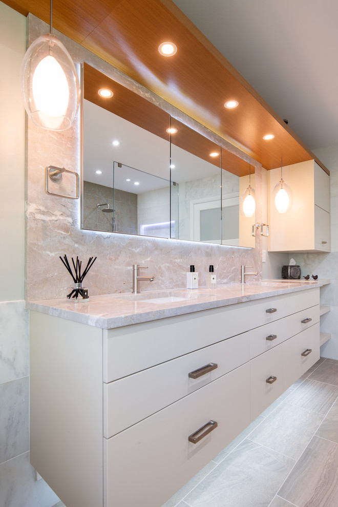 This is an example of a large contemporary master bathroom in DC Metro with flat-panel cabinets, beige cabinets, a freestanding tub, a shower/bathtub combo, beige tile, marble, beige walls, linoleum floors, an undermount sink, marble benchtops, beige floor, a hinged shower door, beige benchtops and a one-piece toilet.