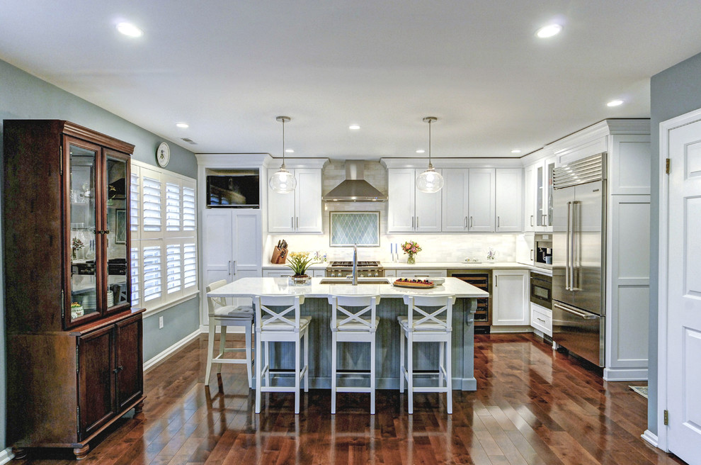 This is an example of a mid-sized transitional l-shaped eat-in kitchen in Philadelphia with an undermount sink, recessed-panel cabinets, white cabinets, marble benchtops, white splashback, marble splashback, stainless steel appliances, medium hardwood floors, with island, brown floor and white benchtop.