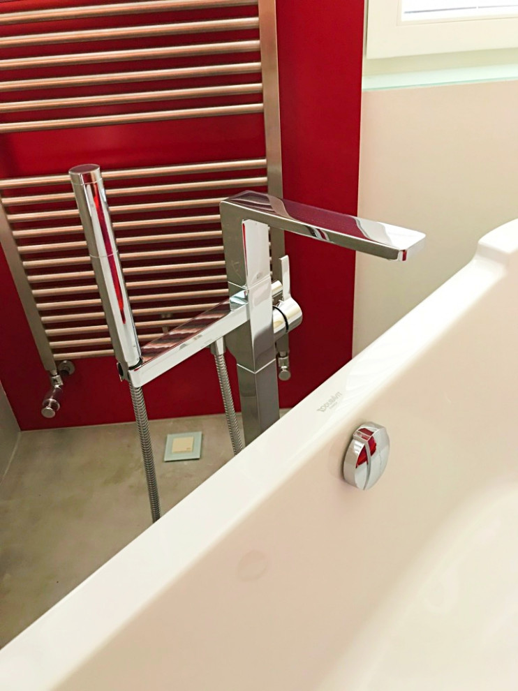 This is an example of a mid-sized contemporary 3/4 bathroom with flat-panel cabinets, red cabinets, a freestanding tub, a curbless shower, a wall-mount toilet, white walls, limestone floors, a vessel sink, solid surface benchtops, beige floor, an open shower, grey benchtops, a double vanity and a built-in vanity.