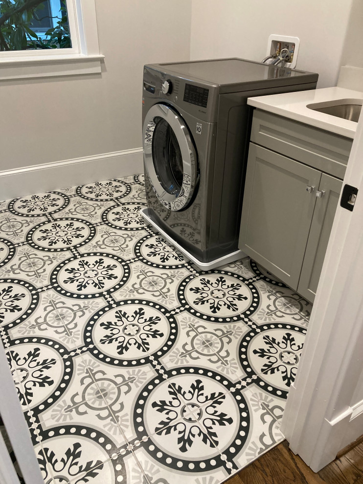 This is an example of a mid-sized transitional single-wall dedicated laundry room in DC Metro with an undermount sink, recessed-panel cabinets, grey cabinets, quartz benchtops, grey walls, porcelain floors, a side-by-side washer and dryer, multi-coloured floor and white benchtop.