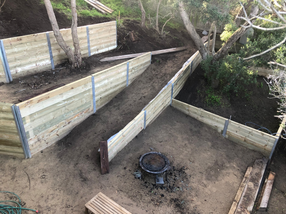 This is an example of an expansive contemporary back formal fully shaded garden for summer in Melbourne with a retaining wall and a wood fence.