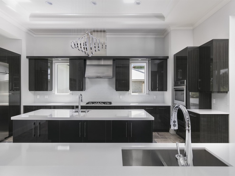 This is an example of a large modern u-shaped separate kitchen in Orlando with an undermount sink, stainless steel appliances, travertine floors, grey floor, flat-panel cabinets, black cabinets, solid surface benchtops, white splashback, glass tile splashback and with island.