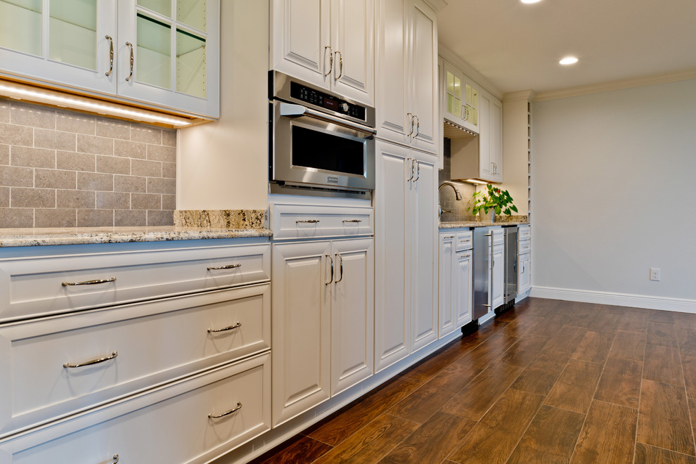 Eat-in kitchen - large transitional galley porcelain tile eat-in kitchen idea in Miami with an undermount sink, raised-panel cabinets, white cabinets, granite countertops, gray backsplash, porcelain backsplash, stainless steel appliances and an island