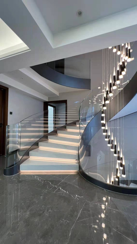 Imagen de escalera curva minimalista grande con escalones de mármol, contrahuellas de mármol, barandilla de vidrio y ladrillo