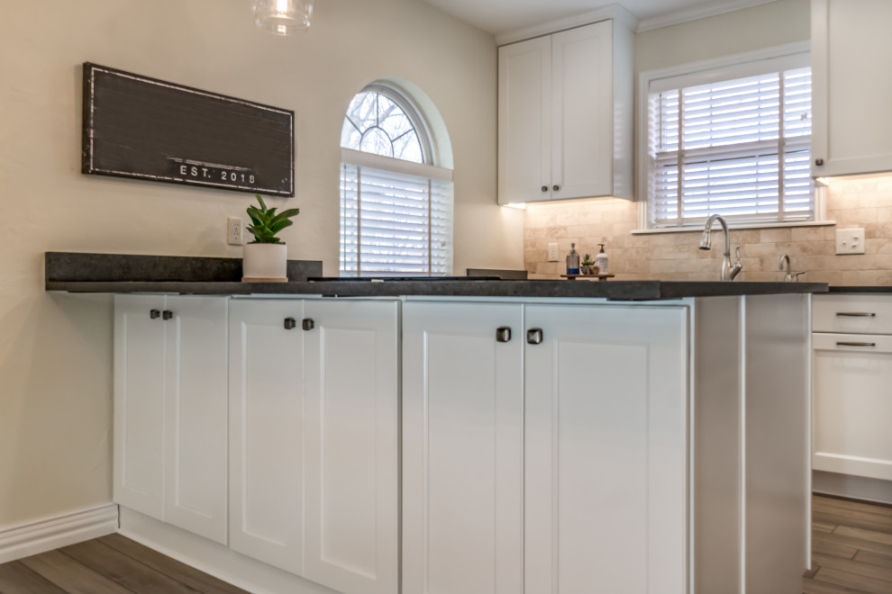 Transitional galley vinyl floor and beige floor eat-in kitchen photo with a double-bowl sink, recessed-panel cabinets, white cabinets, granite countertops, beige backsplash, travertine backsplash, stainless steel appliances, a peninsula and black countertops