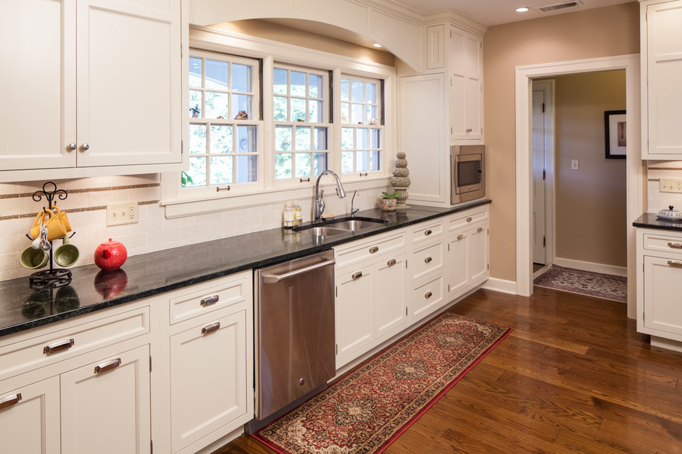Enclosed kitchen - mid-sized transitional single-wall medium tone wood floor enclosed kitchen idea with an undermount sink, beaded inset cabinets, white cabinets, granite countertops, white backsplash, porcelain backsplash, stainless steel appliances and no island