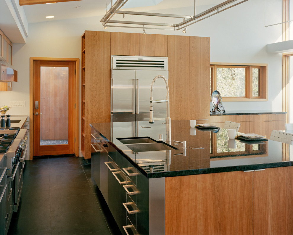 Mid-sized modern l-shaped eat-in kitchen in San Francisco with a double-bowl sink, flat-panel cabinets, medium wood cabinets, granite benchtops, metallic splashback, metal splashback, stainless steel appliances, with island, porcelain floors, black floor, black benchtop and exposed beam.