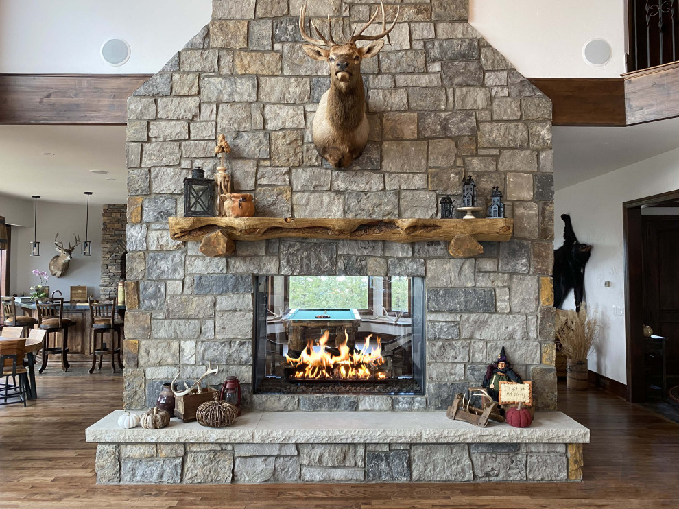 Large elegant enclosed medium tone wood floor, brown floor and vaulted ceiling living room photo in Denver with a bar, white walls, a two-sided fireplace, a stacked stone fireplace and no tv