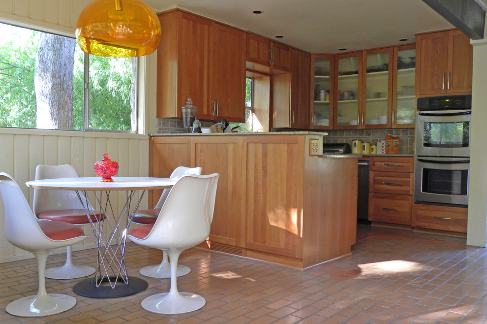 Inspiration for a midcentury eat-in kitchen in Dallas with glass-front cabinets, medium wood cabinets, grey splashback, stainless steel appliances and brick floors.