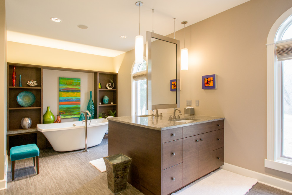 This is an example of a mid-sized contemporary master bathroom in Cedar Rapids with flat-panel cabinets, dark wood cabinets, a freestanding tub, beige walls, porcelain floors, an undermount sink, beige tile, granite benchtops, brown floor, grey benchtops, a double vanity and a built-in vanity.