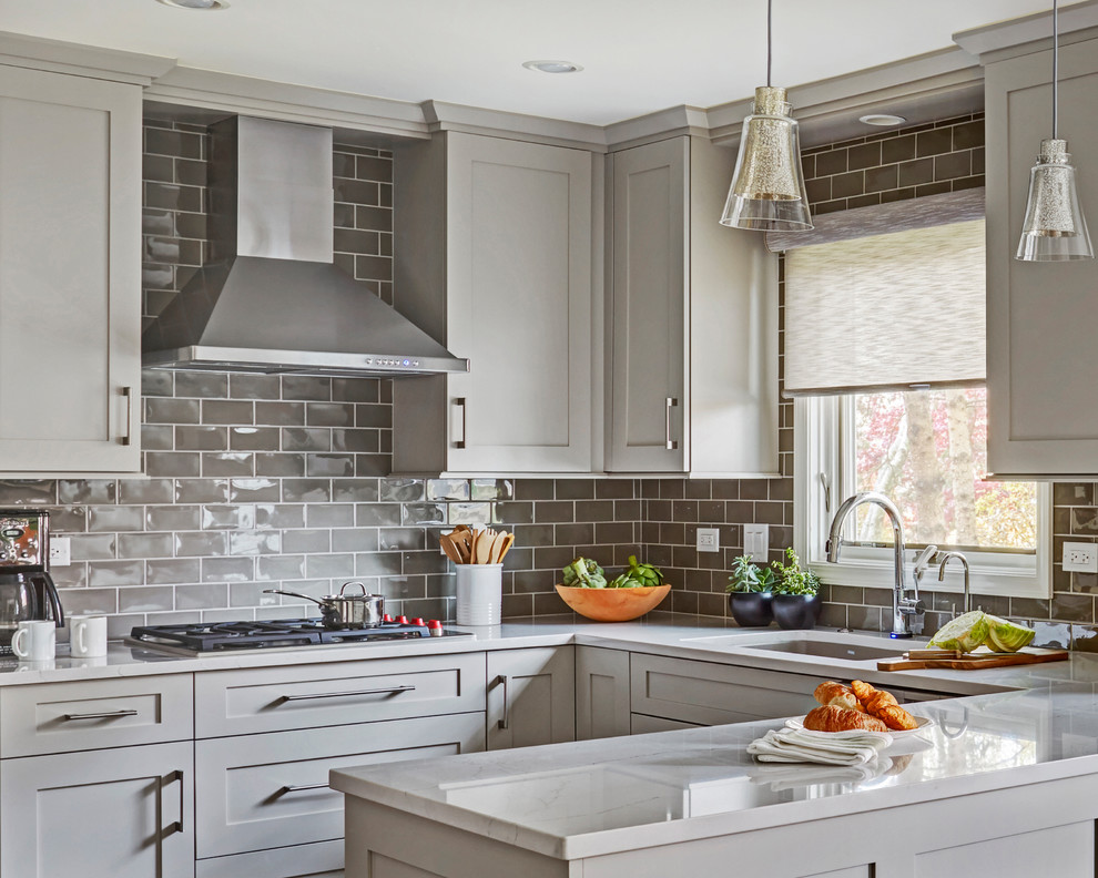 This is an example of a mid-sized transitional u-shaped eat-in kitchen in Chicago with an undermount sink, shaker cabinets, white cabinets, quartz benchtops, grey splashback, subway tile splashback, panelled appliances, medium hardwood floors, a peninsula, brown floor and white benchtop.