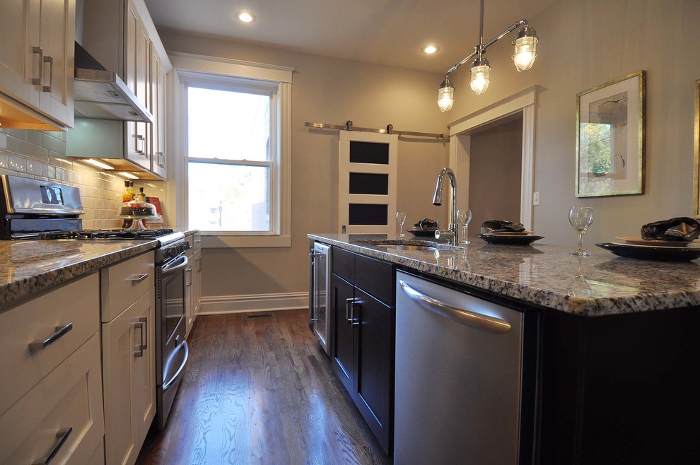 Mid-sized transitional galley medium tone wood floor enclosed kitchen photo in St Louis with an undermount sink, shaker cabinets, granite countertops, white backsplash, subway tile backsplash, stainless steel appliances, an island and white cabinets
