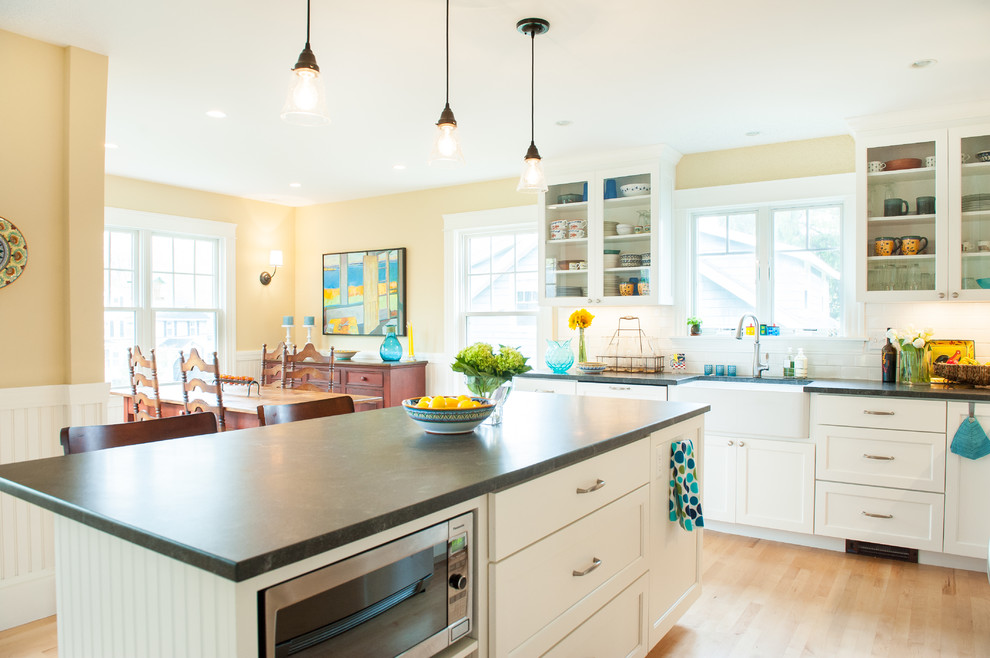 Traditional eat-in kitchen in Portland Maine with a farmhouse sink, glass-front cabinets, white splashback and stainless steel appliances.