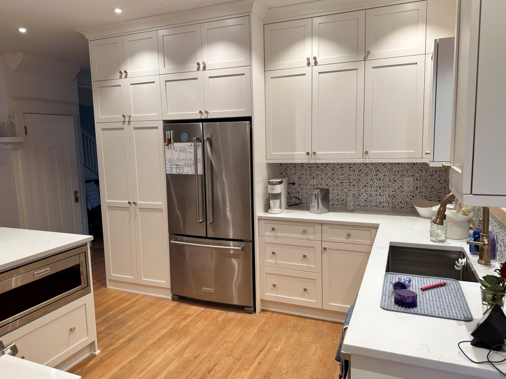 Example of a mid-sized transitional u-shaped medium tone wood floor enclosed kitchen design in Seattle with shaker cabinets, white cabinets, quartz countertops, stainless steel appliances, a peninsula and white countertops
