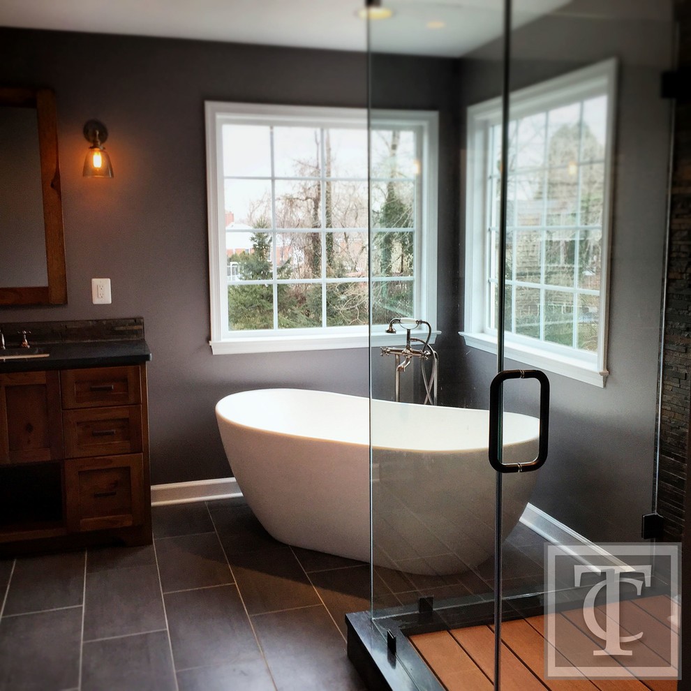 Mid-sized country master bathroom in Baltimore with an undermount sink, shaker cabinets, medium wood cabinets, soapstone benchtops, a freestanding tub, a double shower, a two-piece toilet, gray tile, stone tile, grey walls and porcelain floors.