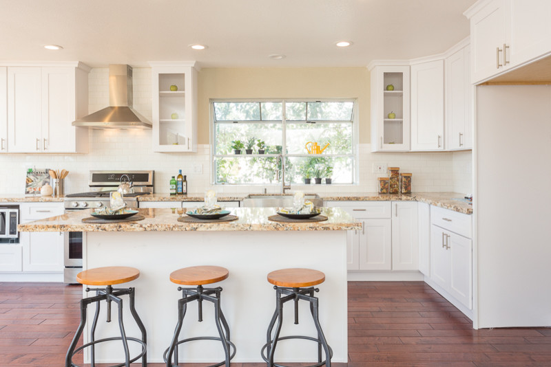 Mid-sized contemporary l-shaped eat-in kitchen in San Francisco with a farmhouse sink, shaker cabinets, white cabinets, granite benchtops, white splashback, ceramic splashback, stainless steel appliances, dark hardwood floors and with island.