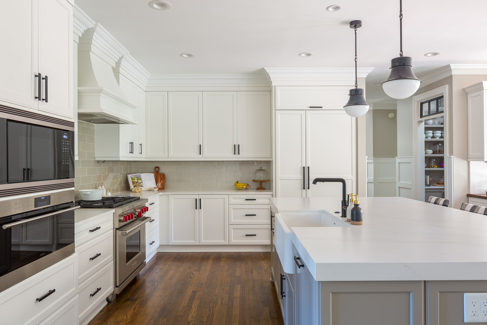 Design ideas for a transitional l-shaped eat-in kitchen in Raleigh with quartz benchtops, with island, white benchtop, a farmhouse sink, recessed-panel cabinets, white cabinets, beige splashback, subway tile splashback, panelled appliances, medium hardwood floors and brown floor.