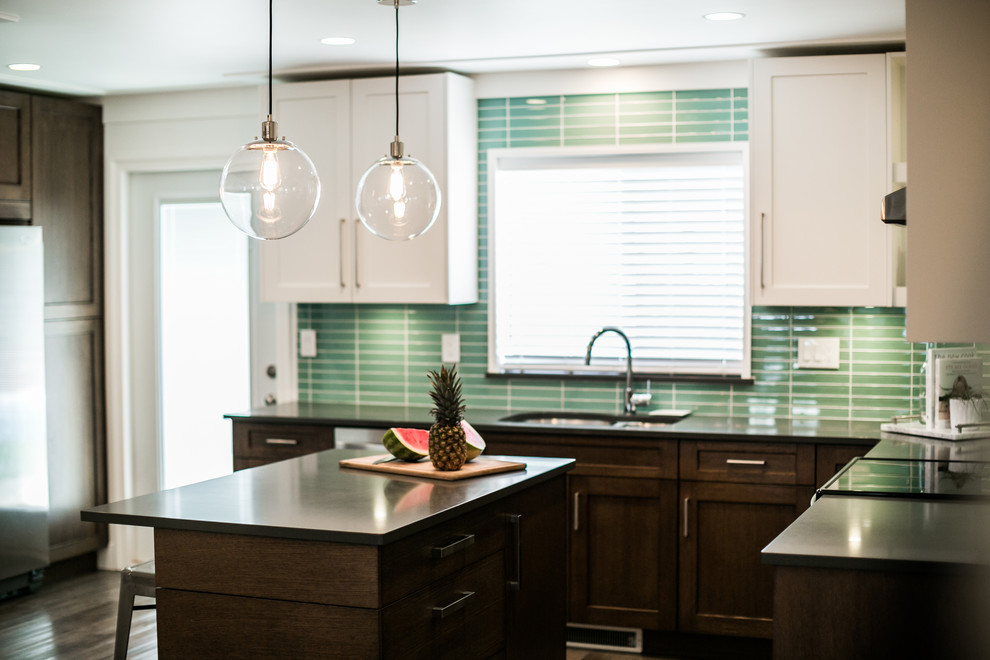 Example of a mid-sized transitional u-shaped dark wood floor and brown floor enclosed kitchen design in Vancouver with flat-panel cabinets, dark wood cabinets, glass tile backsplash, an island, a double-bowl sink, stainless steel appliances and blue backsplash