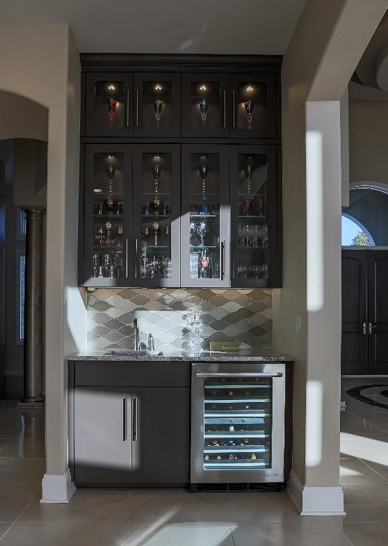 Photo of a small mediterranean single-wall wet bar in Omaha with an undermount sink, flat-panel cabinets, brown cabinets, granite benchtops, multi-coloured splashback, ceramic splashback, travertine floors, beige floor and multi-coloured benchtop.