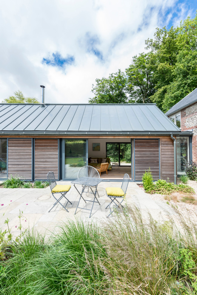 Cette image montre une façade de maison design en bois et planches et couvre-joints de taille moyenne et de plain-pied avec un toit à deux pans, un toit en métal et un toit gris.