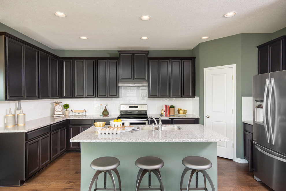 Kitchen - transitional u-shaped medium tone wood floor and brown floor kitchen idea with an undermount sink, recessed-panel cabinets, dark wood cabinets, white backsplash, subway tile backsplash, stainless steel appliances, an island and gray countertops