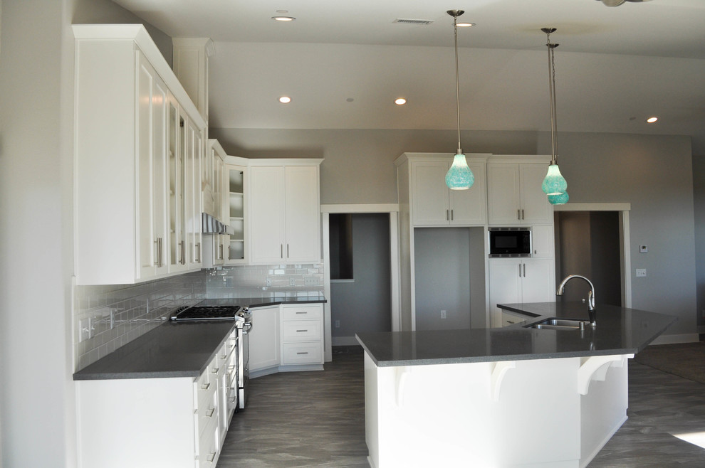 Open concept kitchen - mid-sized transitional l-shaped medium tone wood floor and gray floor open concept kitchen idea with a double-bowl sink, shaker cabinets, white cabinets, quartzite countertops, white backsplash, subway tile backsplash, stainless steel appliances and an island