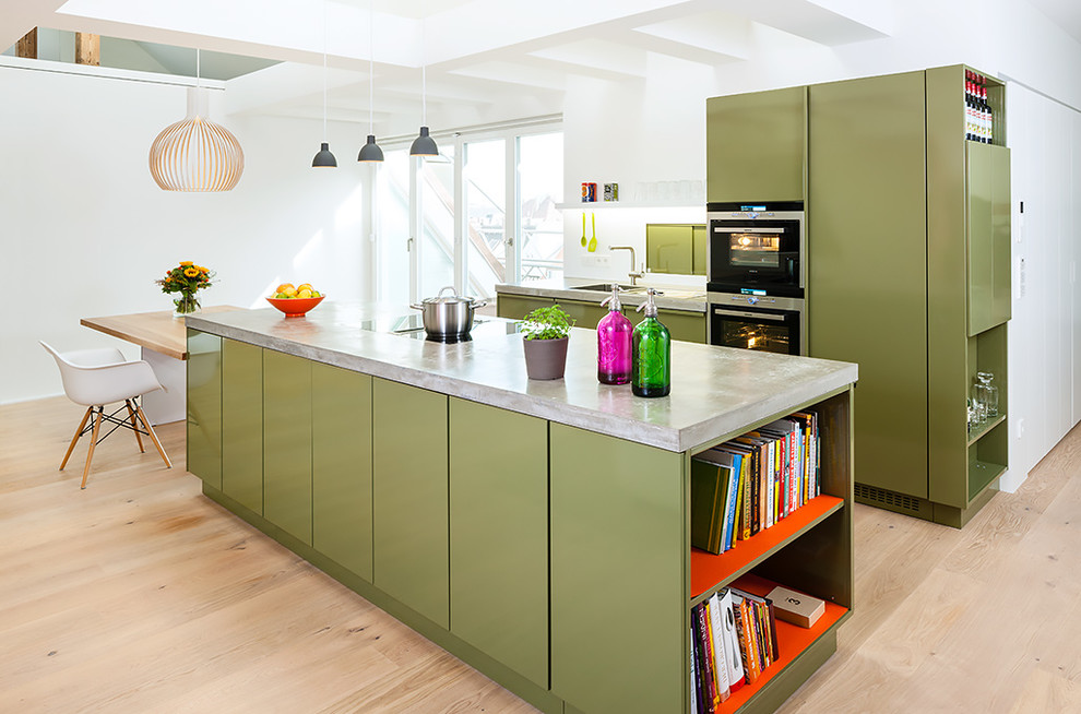 Photo of a large contemporary single-wall open plan kitchen in Berlin with a drop-in sink, flat-panel cabinets, green cabinets, concrete benchtops, white splashback, panelled appliances, light hardwood floors, with island and brown floor.