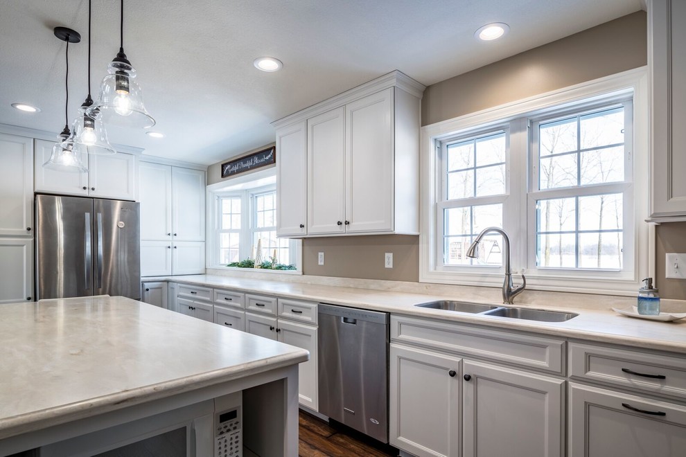 Eat-in kitchen - large transitional l-shaped eat-in kitchen idea with an undermount sink, recessed-panel cabinets, white cabinets, solid surface countertops, gray backsplash, stainless steel appliances and an island