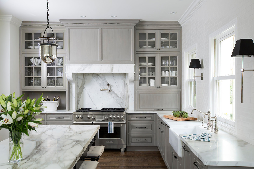 Design ideas for a transitional l-shaped kitchen in San Francisco with a farmhouse sink, recessed-panel cabinets, grey cabinets, white splashback, stone slab splashback, stainless steel appliances, dark hardwood floors, with island, brown floor and white benchtop.