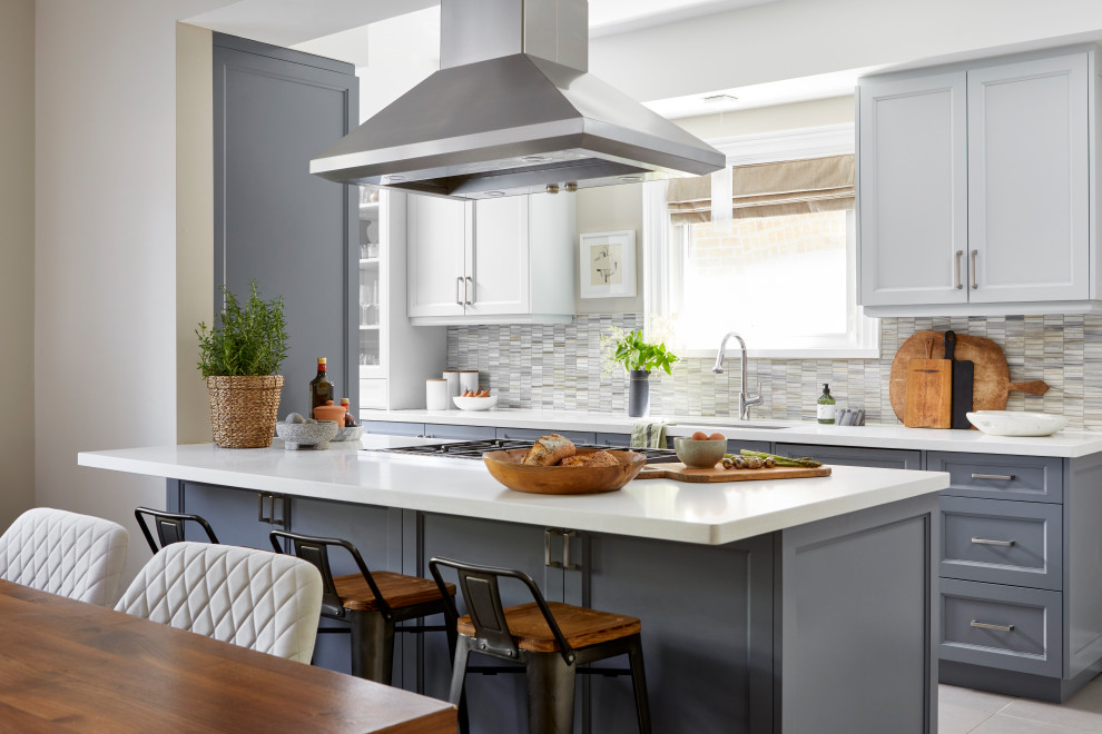 This is an example of a medium sized traditional galley kitchen/diner in Toronto with a submerged sink, shaker cabinets, grey cabinets, engineered stone countertops, multi-coloured splashback, marble splashback, integrated appliances, porcelain flooring, a breakfast bar, grey floors and white worktops.