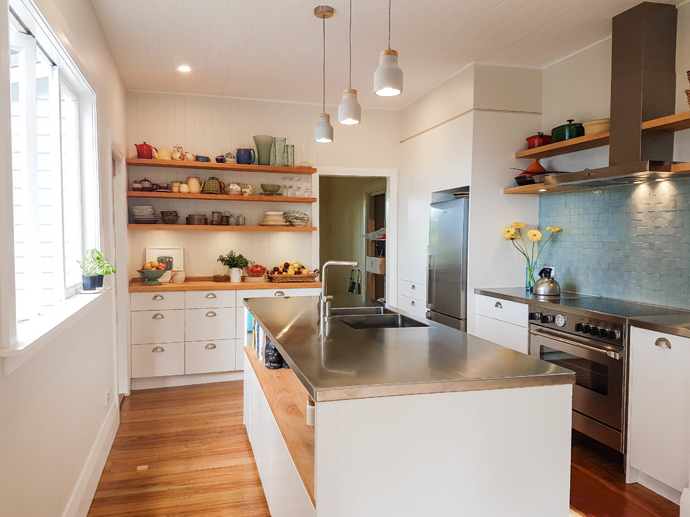 Inspiration for a mid-sized transitional kitchen in Auckland with an integrated sink, white cabinets, stainless steel benchtops, blue splashback, ceramic splashback, stainless steel appliances, medium hardwood floors and with island.