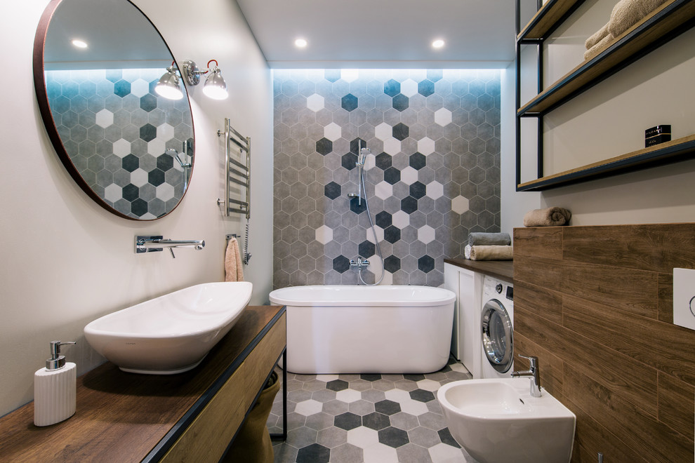 Photo of a small transitional master bathroom in Other with flat-panel cabinets, medium wood cabinets, a freestanding tub, a wall-mount toilet, gray tile, ceramic tile, grey walls, ceramic floors, a drop-in sink, laminate benchtops and grey floor.