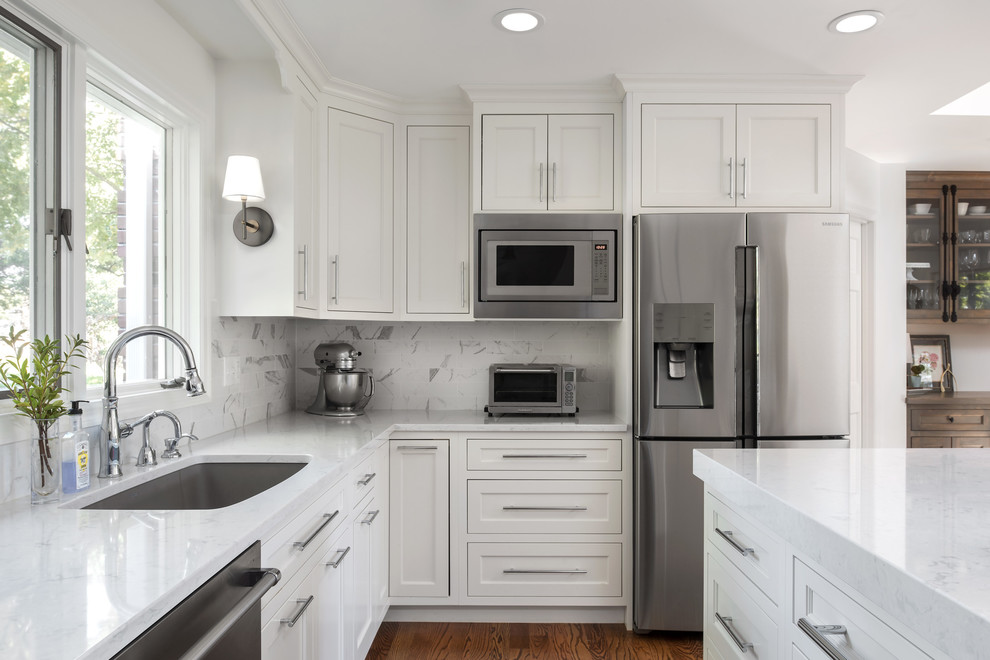 Inspiration for a mid-sized transitional u-shaped medium tone wood floor and brown floor eat-in kitchen remodel in St Louis with a single-bowl sink, flat-panel cabinets, white cabinets, quartz countertops, ceramic backsplash, stainless steel appliances and an island