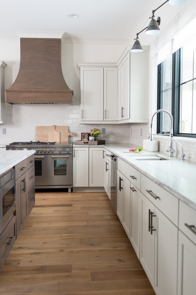Inspiration for a mid-sized transitional l-shaped separate kitchen in Indianapolis with an undermount sink, shaker cabinets, white cabinets, white splashback, stainless steel appliances, medium hardwood floors and with island.