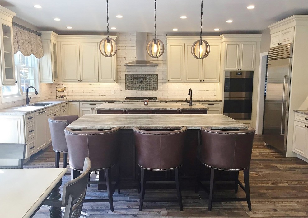 Large country l-shaped open plan kitchen in Philadelphia with an undermount sink, raised-panel cabinets, distressed cabinets, quartzite benchtops, white splashback, ceramic splashback, stainless steel appliances, porcelain floors, multiple islands, brown floor and multi-coloured benchtop.