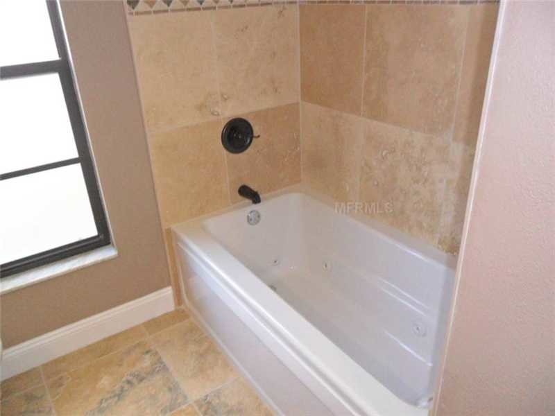 Mid-sized country 3/4 bathroom in Tampa with an undermount sink, shaker cabinets, light wood cabinets, solid surface benchtops, a drop-in tub, a shower/bathtub combo, a one-piece toilet, beige walls and ceramic floors.