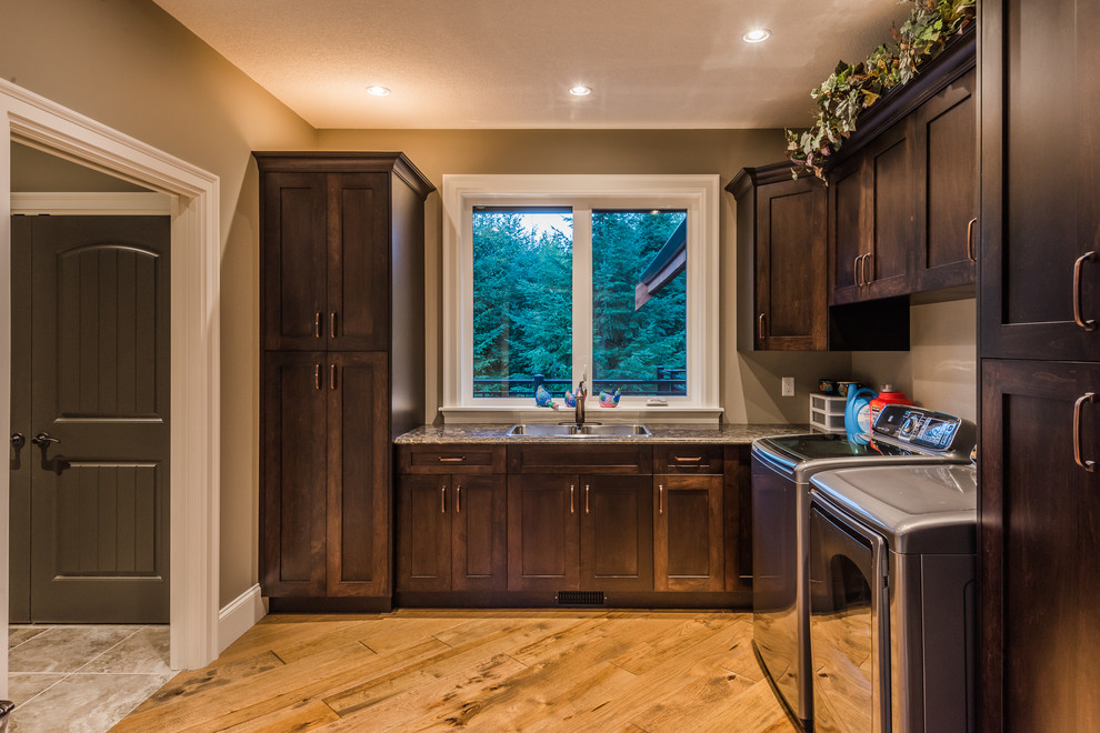 Inspiration for a mid-sized country u-shaped dedicated laundry room with a double-bowl sink, dark wood cabinets, granite benchtops, beige walls, medium hardwood floors, a side-by-side washer and dryer and recessed-panel cabinets.