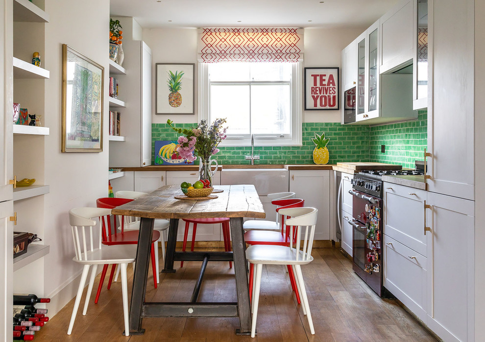 Mid-sized eclectic l-shaped eat-in kitchen in London with a farmhouse sink, shaker cabinets, white cabinets, wood benchtops, green splashback, ceramic splashback, stainless steel appliances, medium hardwood floors, no island, brown floor and brown benchtop.