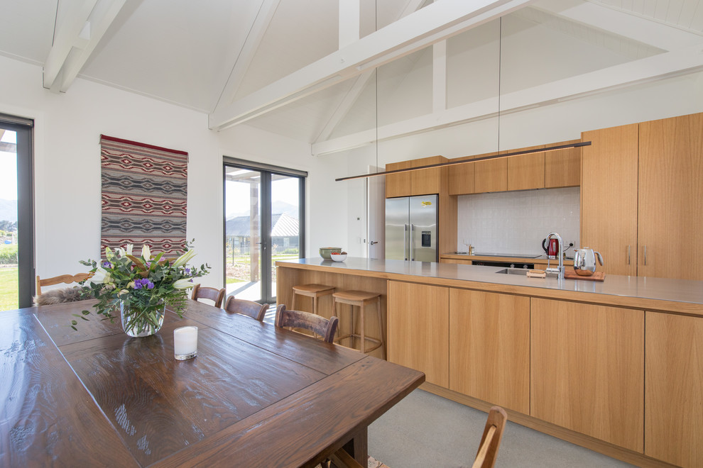 Inspiration for a country galley open plan kitchen in Other with an undermount sink, flat-panel cabinets, medium wood cabinets, white splashback, stainless steel appliances, with island and grey floor.